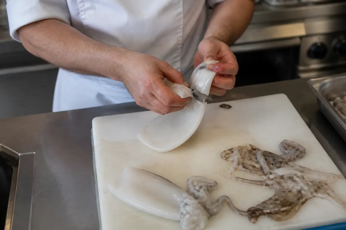 Personne préparant des seiches sur planche pour cuisiner des seiches en cuisine professionnelle